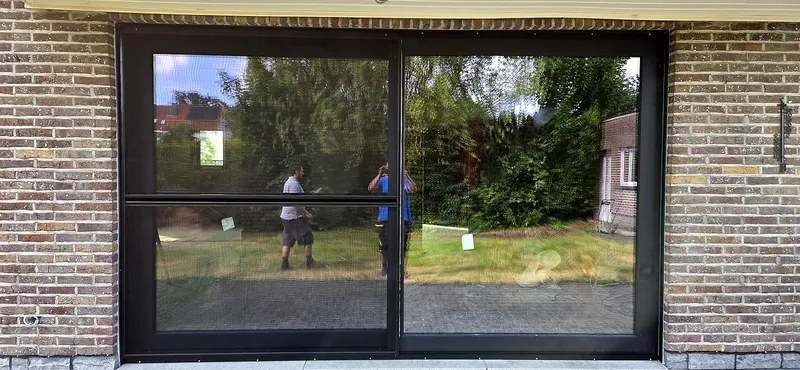 Baie vitrée coulissante à profilés aluminium anthracite, posée dans une façade en briques