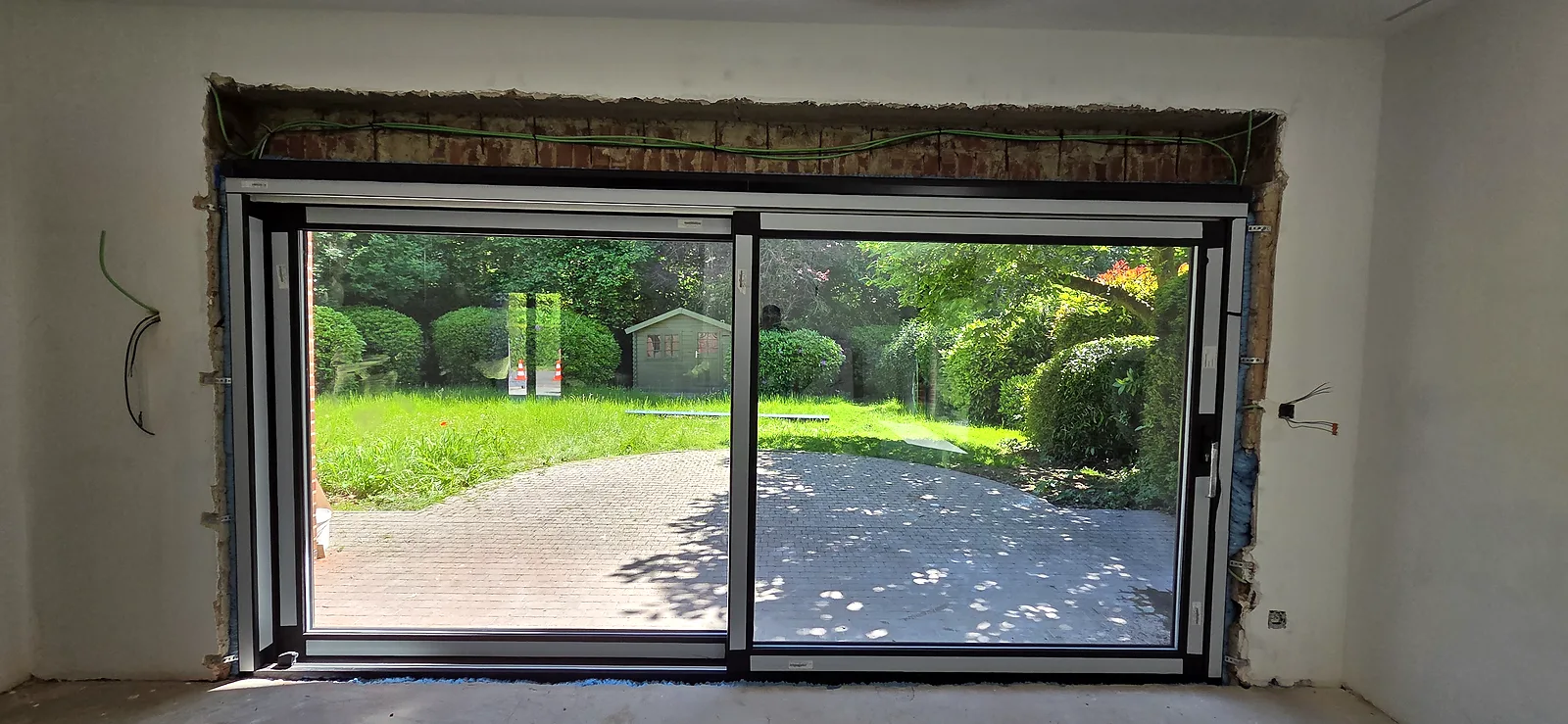 Baie coulissante aluminium à deux vantaux vue de l'intérieur, donnant sur un jardin, pose fraîchement posée