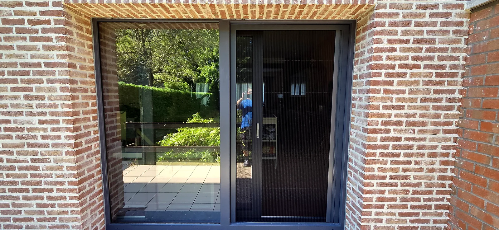 Baie coulissante aluminium à profilés fins, posée dans une façade en briques, vue sur la terrasse