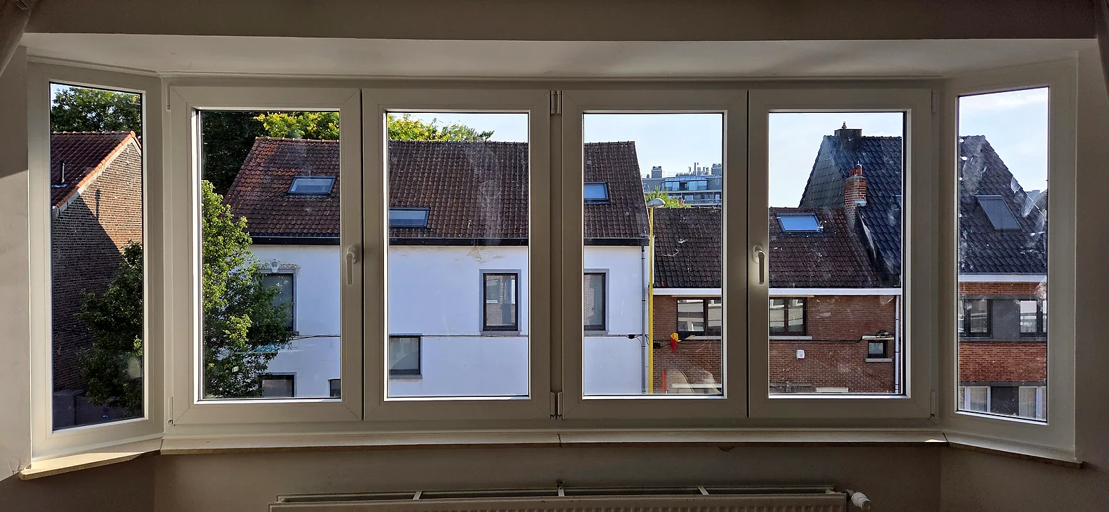Baie en oriel PVC blanc à plusieurs vantaux, posée en applique, vue dégagée sur les toitures du quartier
