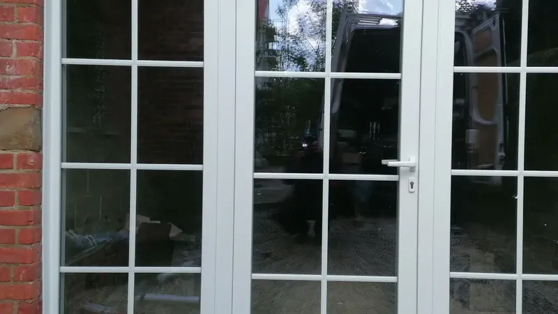 Porte-fenêtre PVC blanche à petits bois, posée dans une façade en briques