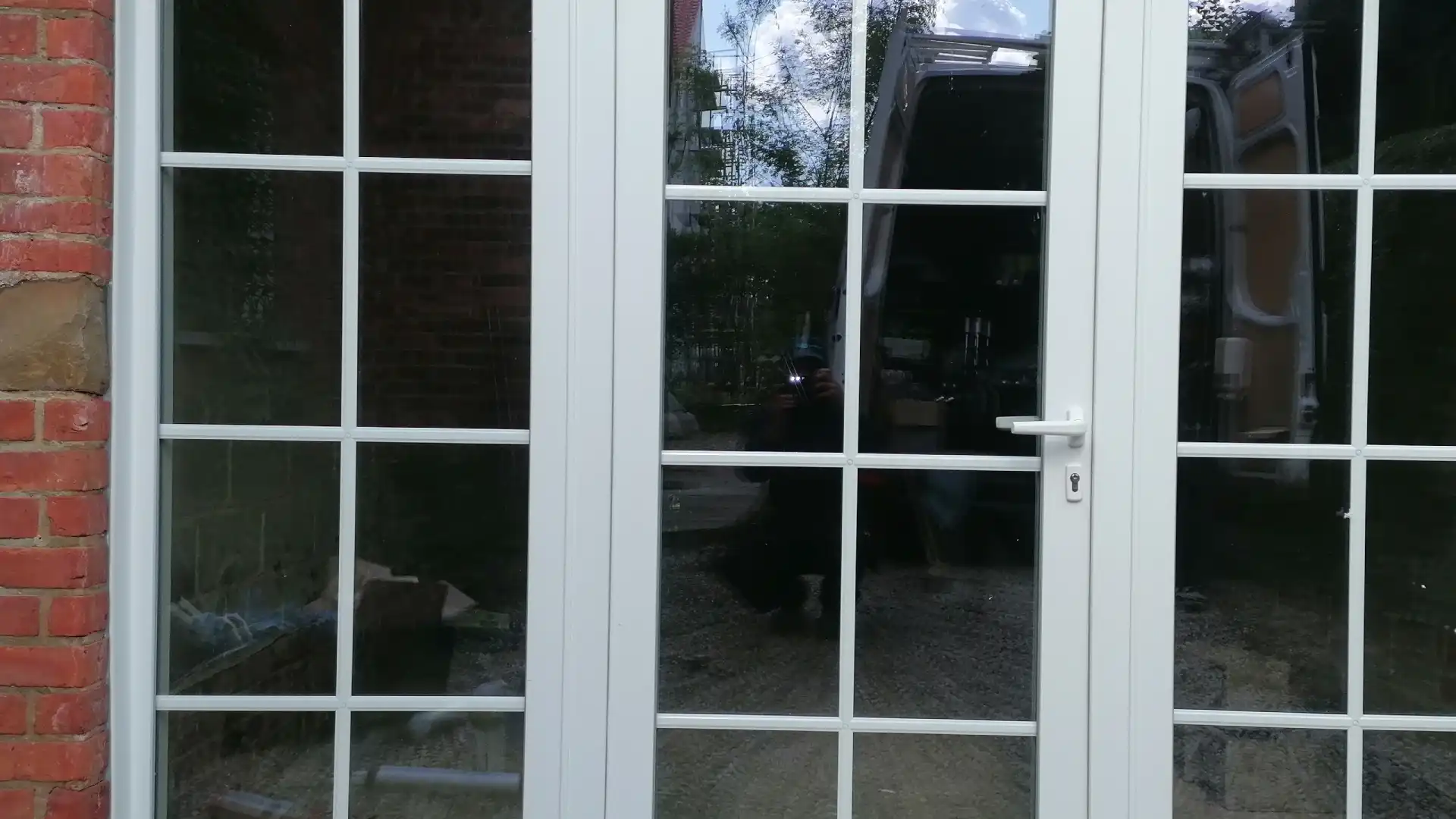 Porte-fenêtre PVC blanche à petits bois, posée dans une façade en briques