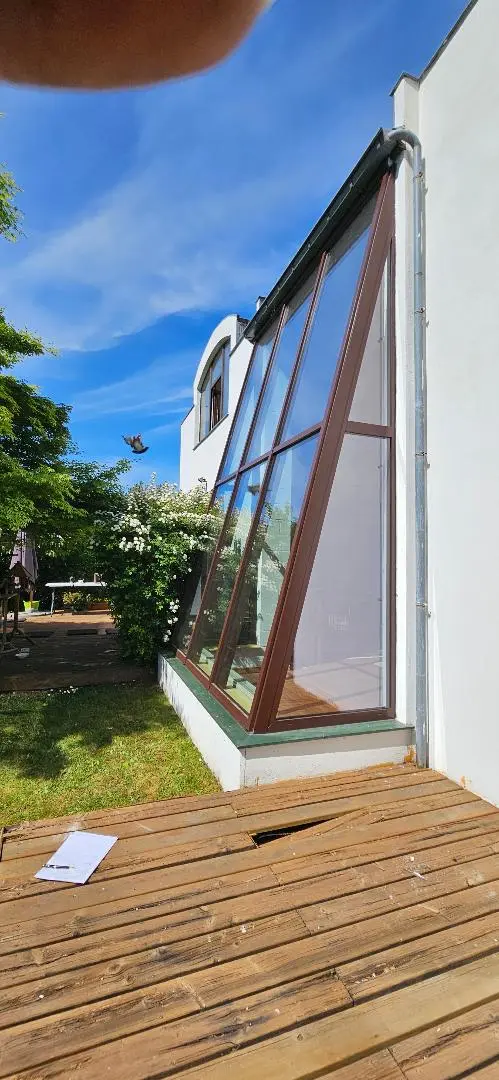 Extension vitrée à pans inclinés, profilés bruns, ouverte sur une terrasse en bois