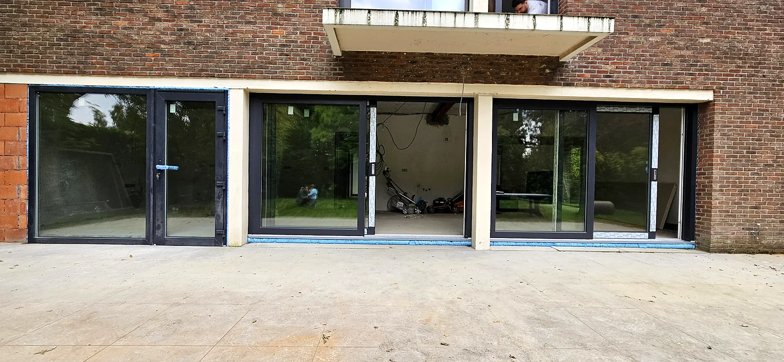 Façade en briques avec trois baies coulissantes en aluminium noir, encore protégées par le film de chantier