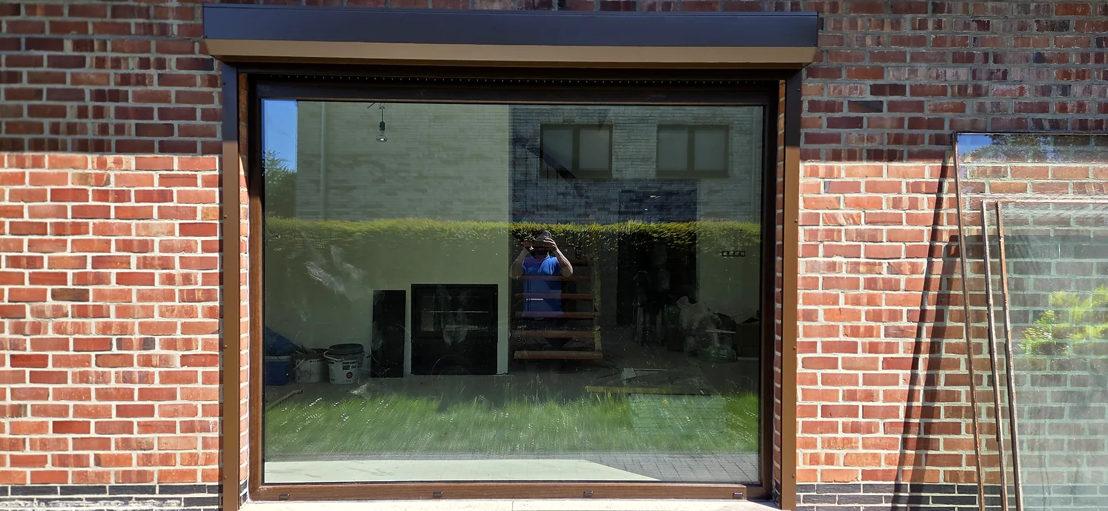 Grande fenêtre fixe à profilé brun posée en façade de brique, surmontée d'un volet roulant à coffre apparent