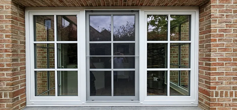 Fenêtres et porte coulissante en PVC blanc à petits-bois, posées dans une façade en briques avec vue sur le jardin