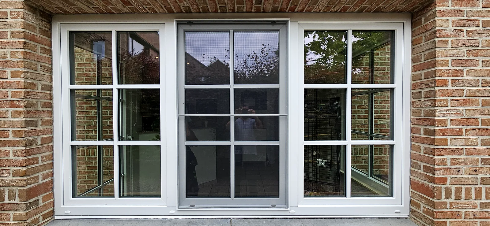 Porte-fenêtre PVC blanche à petits-bois encadrée de deux fenêtres jumelées, façade en briques