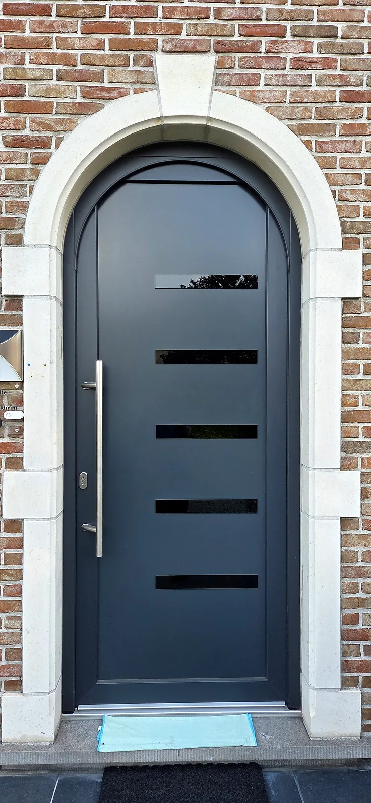 Porte d'entrée cintrée anthracite, encadrement en pierre, façade en briques