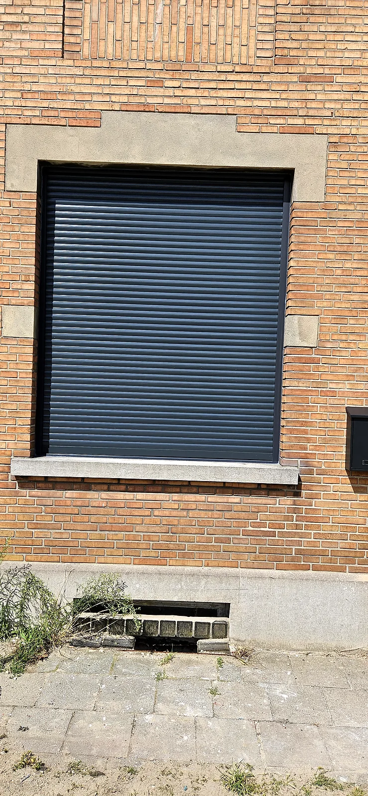Volet roulant anthracite fermé sur une fenêtre, façade en briques